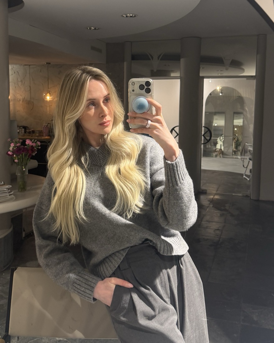 Marinka Essel taking a mirror selfie in a grey knit sweater